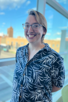 Ash wearing a floral blue shirt and glasses smiling at camera.