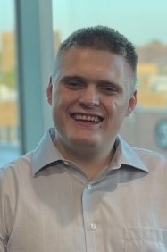 Matthew smiles at the camera wearing a tan button down shirt.