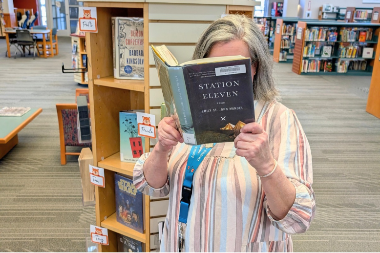Staff member stands next to a display with their face buried in a book.