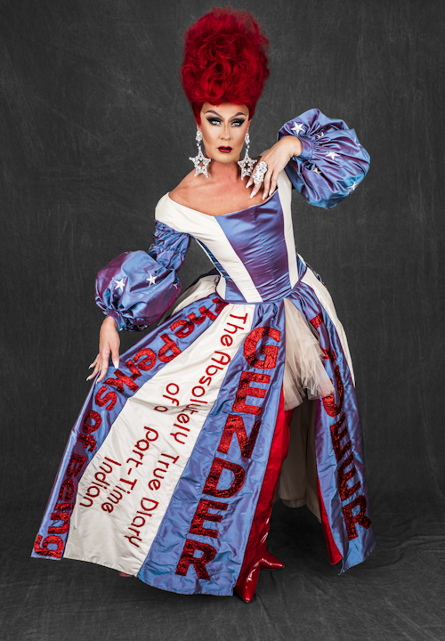 Drag Queen with tall red hair and large star earrings modeling the red, white, and blue gown.