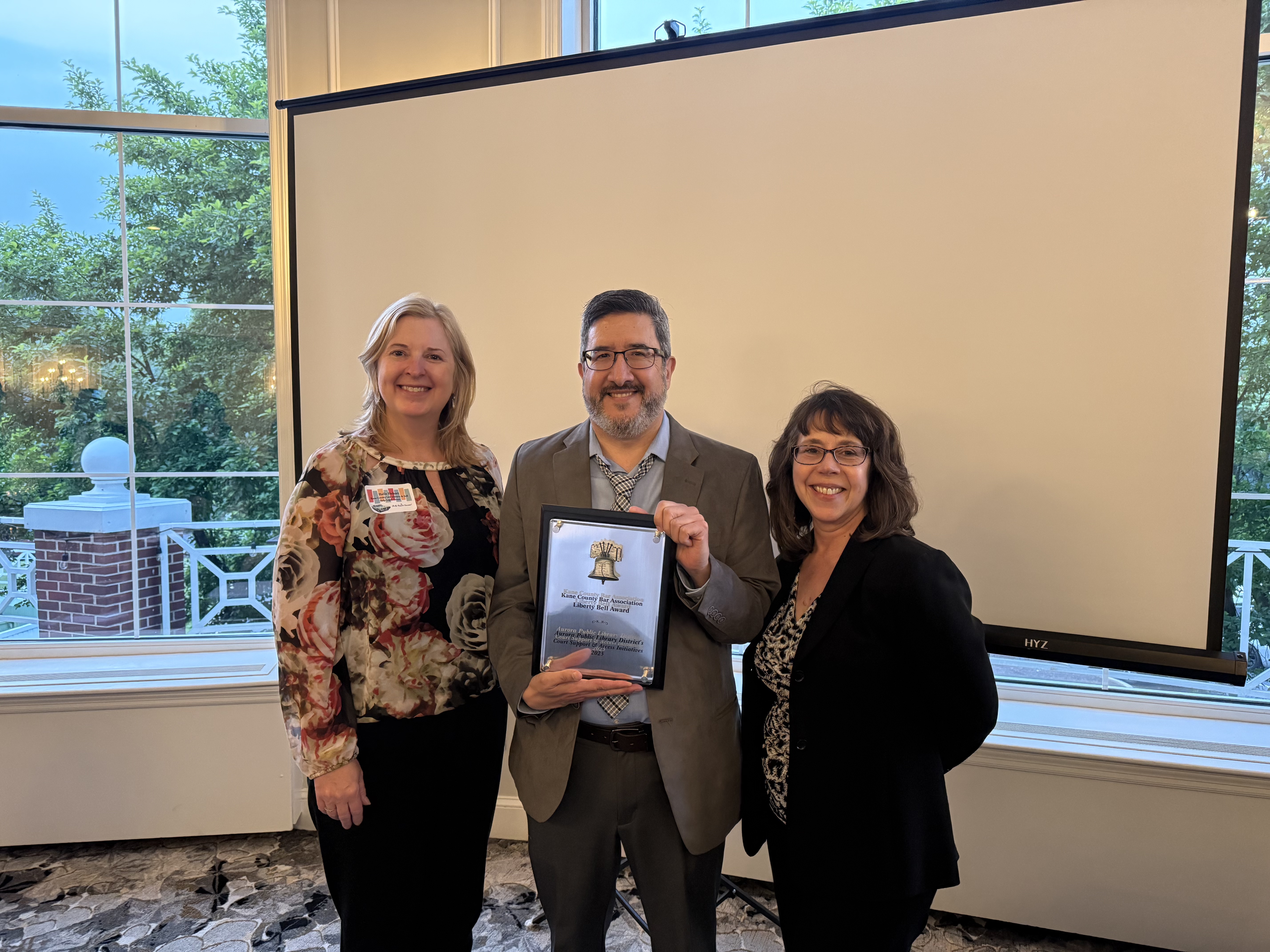 Representative from the Kane County Law Library poses with APLD staff Eric and Michaela with the award plaque.