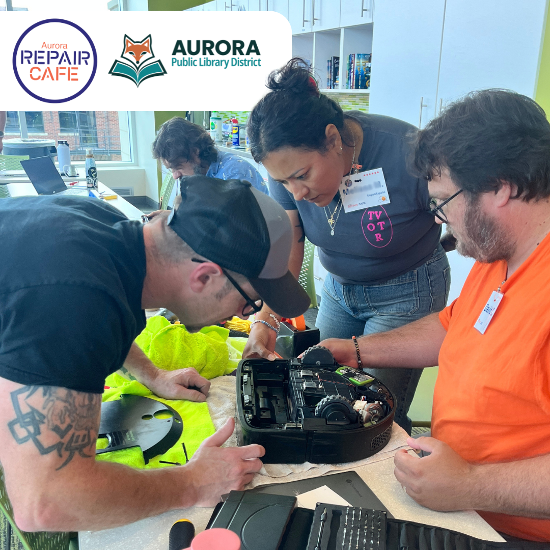 Volunteers work with their heads close together to repair a robot vacuum.