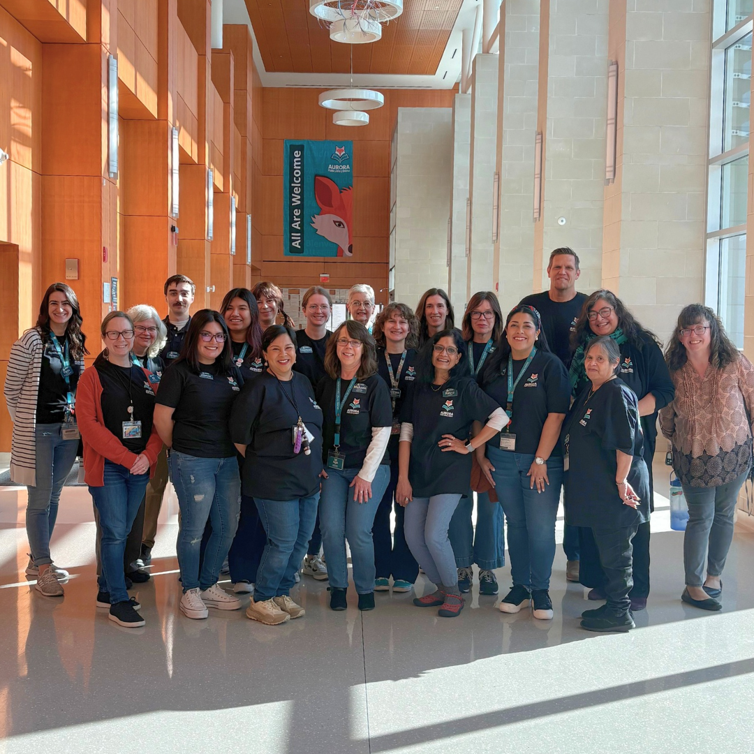 Group photo of library staff, many wearing matching APLD shirts, in the Santori Library atrium.
