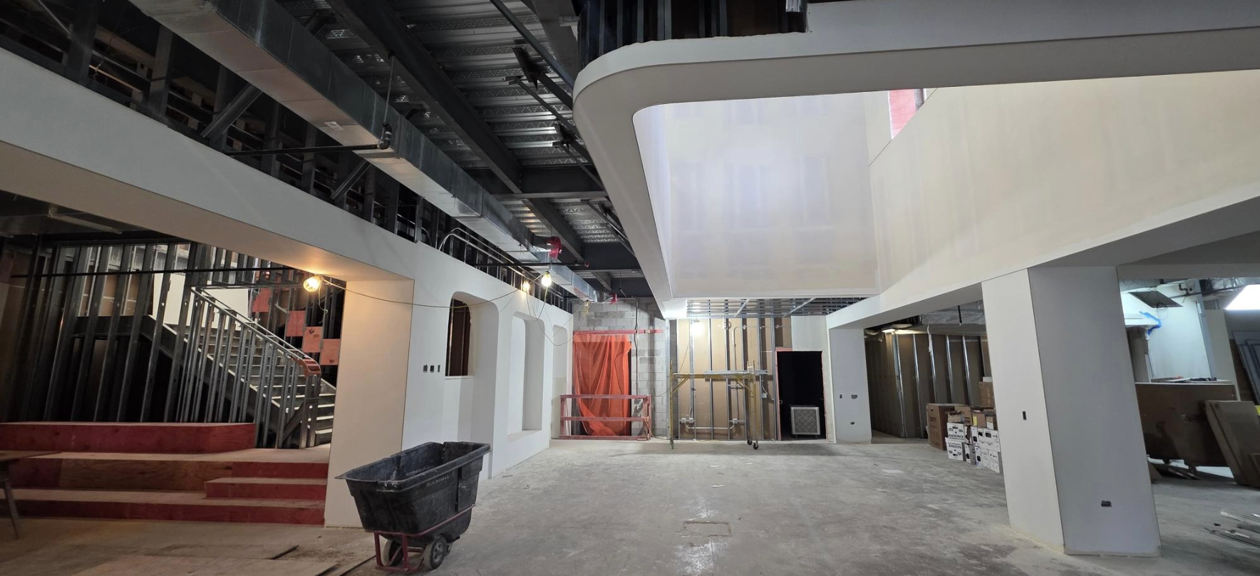 The new lobby displays with new, white drywall. Ceiling exposure to metal with a new rounded ceiling treatment shows. Stairs show on the righthand side.
