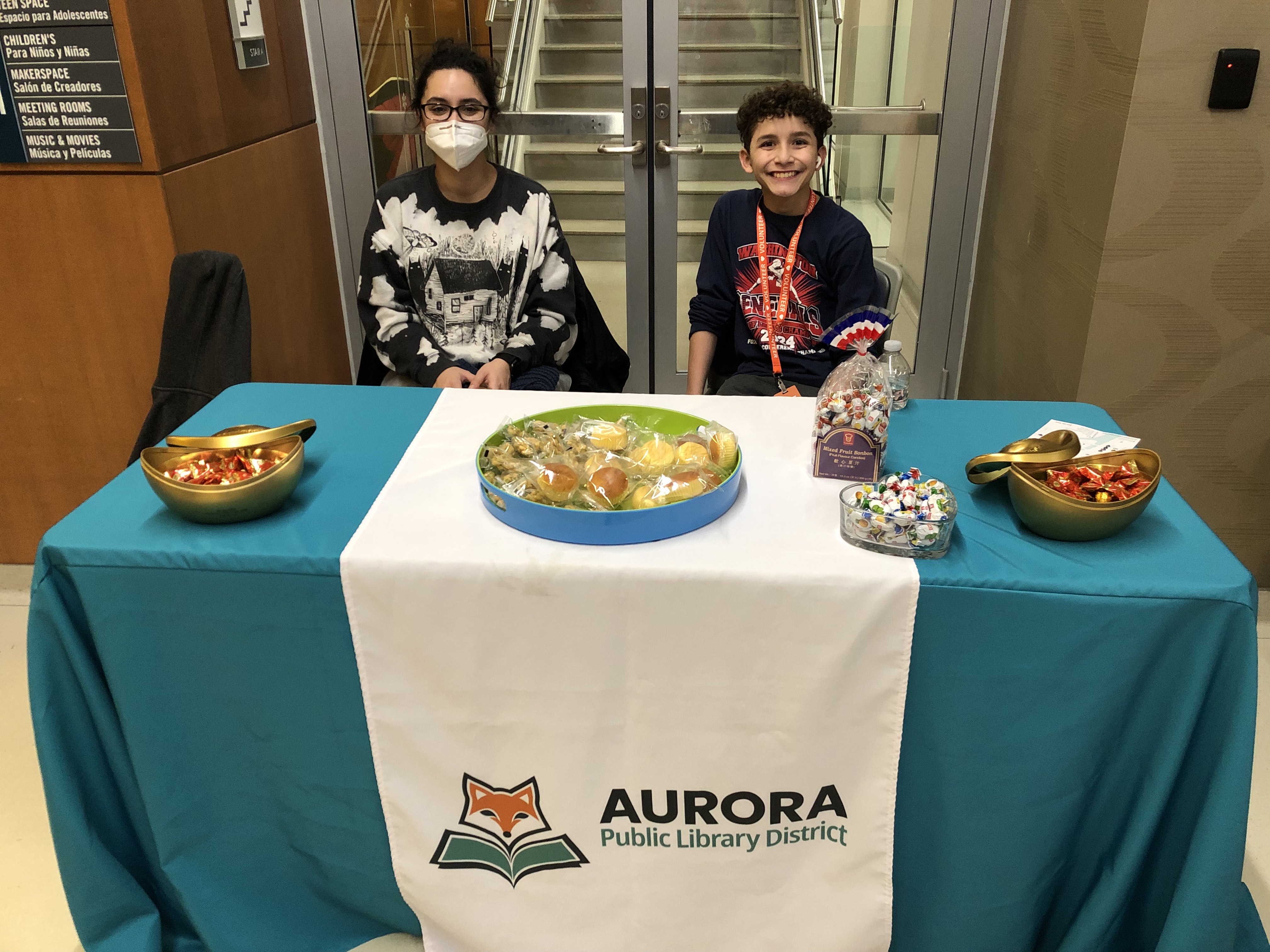 Two teens sit at an APLD table giving away items during an event.